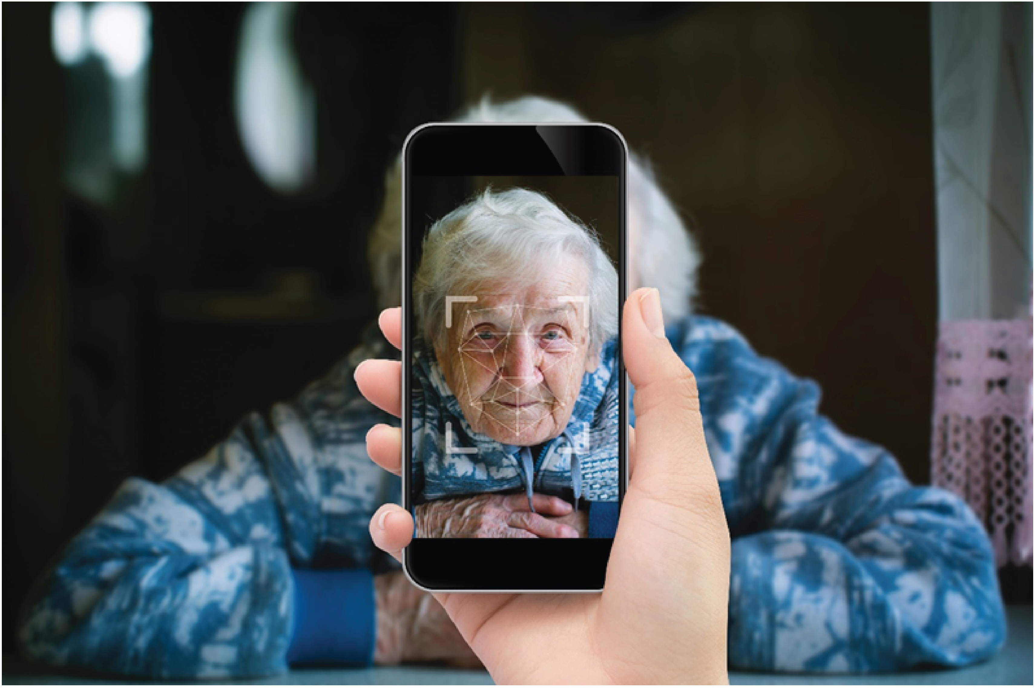 Alt text: A hand holding a cell phone that is taking a video of an older adult’s face using the PainChek app.
