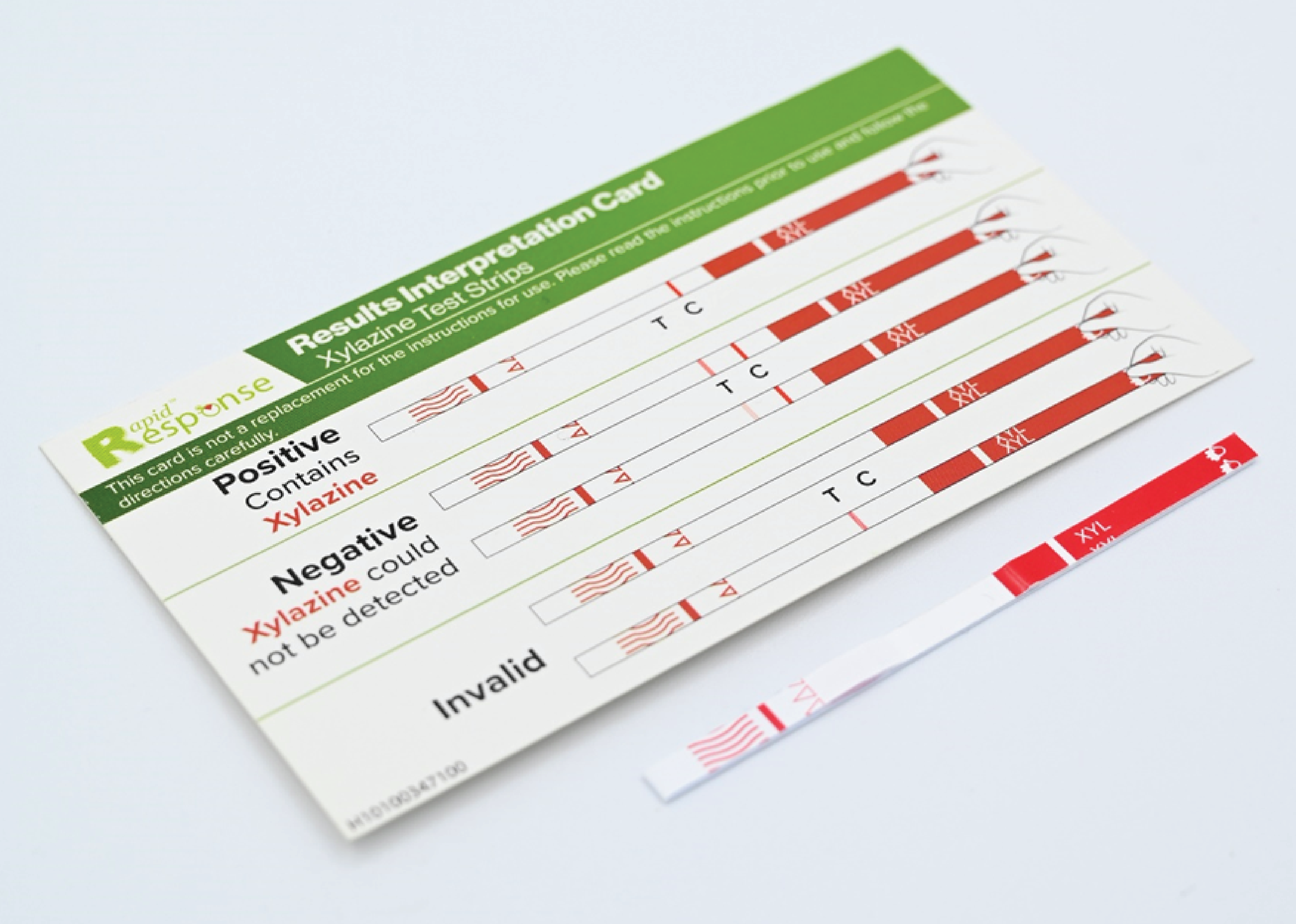 Photograph of a xylazine test strip and a results interpretation card. The interpretation card shows illustrations of test strips that indicate positive, negative, and invalid testing results for xylazine.